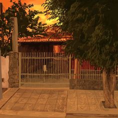 an orange sky is seen behind a fenced in area with a tree and building