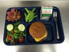 a blue tray topped with a hamburger and veggies next to a carton of milk