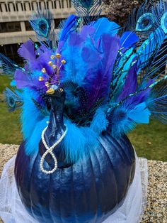 a blue pumpkin with peacock feathers and pearls on it's head is sitting outside