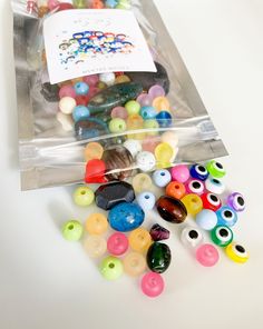 a bag filled with lots of different colored beads on top of a white table next to a card