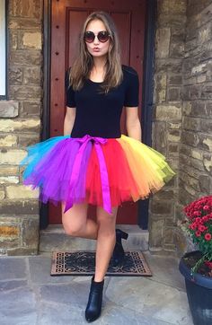 a woman standing in front of a door wearing a rainbow tutu skirt and black shirt