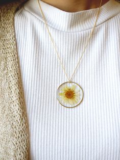 a woman wearing a white sweater with a yellow flower in the center on a gold chain