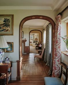 an archway leads into a living room with wood floors and curtains on the windowsill