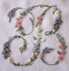 several different types of flowers and leaves on a white table cloth with embroidered thread in the middle