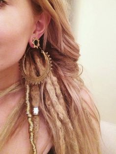 a woman with long blonde hair wearing large gold hoops and braiding her hair