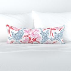 a bed with white sheets and pink flowers on the pillow case, along with two pillows