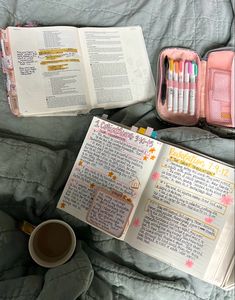 an open bible next to a cup of coffee on a bed with other items in it