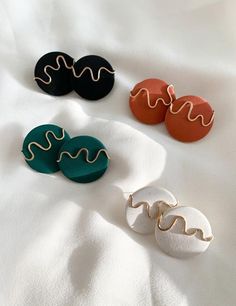 three pairs of earrings sitting on top of a white cloth covered bed next to each other