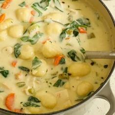 a pot filled with soup and vegetables on top of a stove next to a wooden spoon