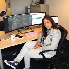 a woman sitting at a desk with two computer monitors and a keyboard in front of her