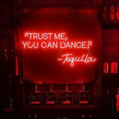 a red neon sign that says trust me you can dance tequila in front of liquor bottles