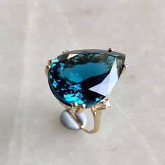 This stunning ring is set in 14k Solid Yellow Gold with Natural London Blue Topaz and Diamond with utmost precision. It is an unique statement gemstone ring for nearly every occasion and is completely hassle-free jewelry. ITEM DETAILS * CENTER GEM: London Blue topaz * GEM SIZE: 21.9X15.5mm * GEM SHAPE: Pear * Gem weight: 21.65 carats * SIDE GEM: Diamond * GEM SIZE: 2mm (2 pcs),  * GEM SHAPE: ROUND * Gem weight: 0.05 carats * Total Gem weight: 21.70 carats * Gold Purity: 14KT * Gold Weight: 3.40 gram * Total Weight of the Ring: 7.74 gram The Gold purity is guaranteed and it comes with authentic 14KT gold hallmark. Since my items are handmade, they are absolutely nickel and lead free. CUSTOMIZATION: * Size Customization is available for this ring and it is available in all ring sizes. Kindly Luxury Classic Polished Topaz Ring, Luxury Hallmarked Collectible Topaz Ring, Topaz Diamond Ring, Blue Topaz Engagement Ring, Topaz Engagement Ring, London Blue Topaz Ring, Gold Gemstone Ring, Emerald Engagement Ring Cut, Solid Gold Ring