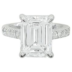 an emerald cut diamond ring with diamonds on the band and shoulders, set in 18k white gold