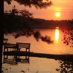 a bench sitting on the edge of a lake at sunset