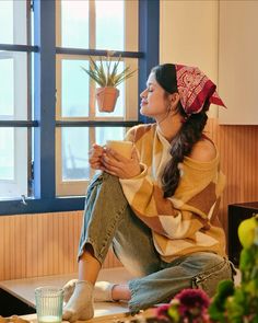 a woman sitting on a window sill with a potted plant in her hand