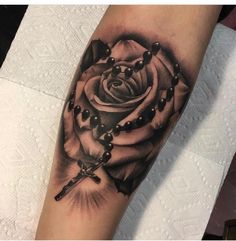 a black and white rose tattoo with rosarys on the arm is featured in this photo