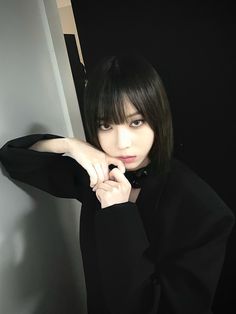 a young woman with black hair and bangs posing for a photo while leaning against a wall