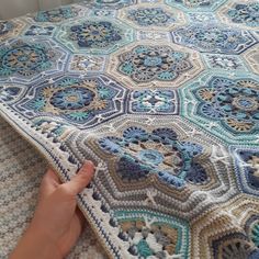 someone is holding up a crocheted blanket on top of a bed with blue and white colors