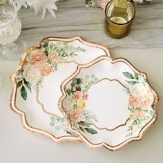 two white and gold plates with flowers on them next to a vase filled with flowers