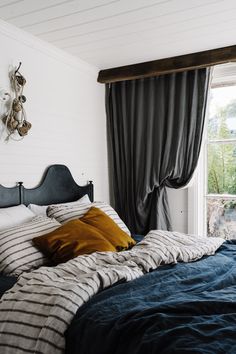 a bed with blue and white sheets in a bedroom next to a window that looks out onto the woods