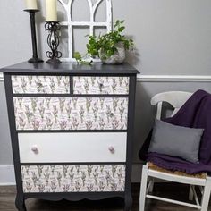 a black and white dresser with flowers on it next to a purple chair in front of a gray wall