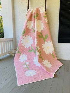 a pink and white flowered blanket sitting on top of a wooden chair next to a window