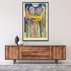 an abstract painting hangs on the wall above a wooden cabinet in a room with white walls