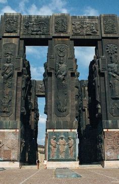 an intricately carved stone gate in the middle of a parking lot with statues on it