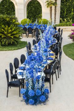 a long table is set with blue flowers and place settings for an elegant dinner party