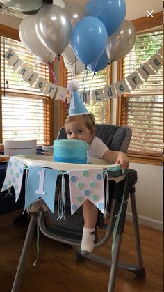 a young child sitting in a high chair with a birthday cake and balloons on the table