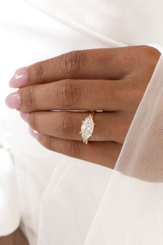 a woman's hand wearing a gold ring with an oval shaped diamond on it