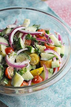 a glass bowl filled with vegetables on top of a blue and white table cloth next to a knife