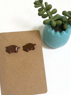 a pair of earrings sitting on top of a piece of paper next to a plant