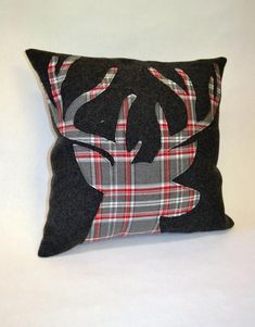 a black pillow with a plaid deer head on the front and back, sitting on a white surface