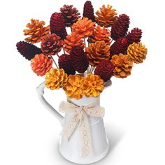 an arrangement of pine cones in a white vase with a bow tied around the top