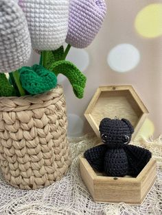 a crocheted teddy bear sitting in a wooden box next to flowers