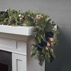 a christmas wreath on top of a fireplace mantel decorated with evergreen and gold bells