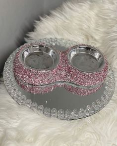 two bowls with pink glitter on them sitting on a white furnishing area next to a furry rug