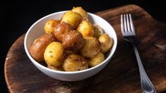 a white bowl filled with fried potatoes on top of a wooden cutting board next to a fork