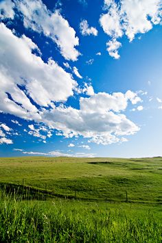 the sky is filled with fluffy clouds over an open green field on a sunny day