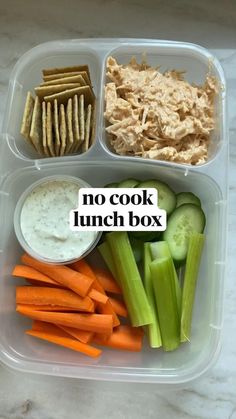 a plastic container filled with vegetables and crackers next to hummus, celery, cucumbers