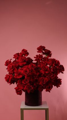 a vase filled with lots of red flowers on top of a wooden table next to a pink wall