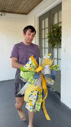 a man is holding a large yellow and green bow on the front door way to his house