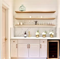 a kitchen with white cabinets and marble counter tops, gold accents on the top shelf