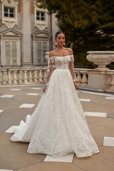 a woman in a white wedding dress standing on a stone walkway with an ornate building behind her