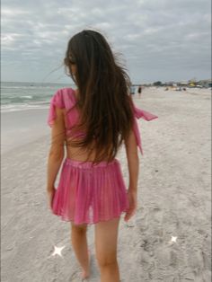 a woman walking on the beach with her back to the camera while wearing a pink dress