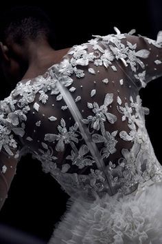 the back of a woman's wedding dress with white flowers and pearls on it