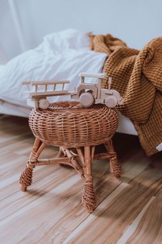 a wicker stool with toy cars on top of it next to a white bed