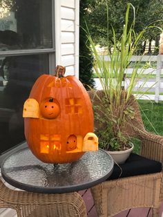 a pumpkin with faces carved into it sitting on top of a table in front of a house