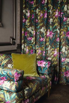 a colorful couch and chair in front of a floral curtain